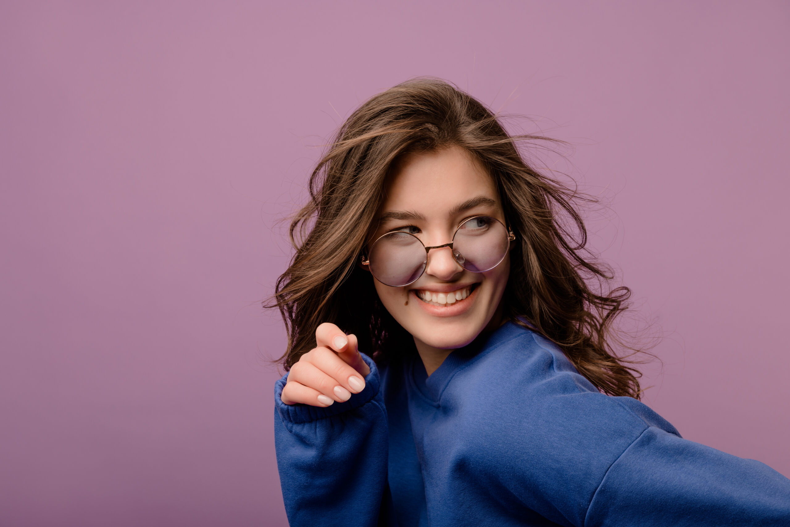 Close-up of pretty young caucasian brunette girl in blue hoodie and glasses looks away in studio. People emotions, lifestyle and fashion concept.