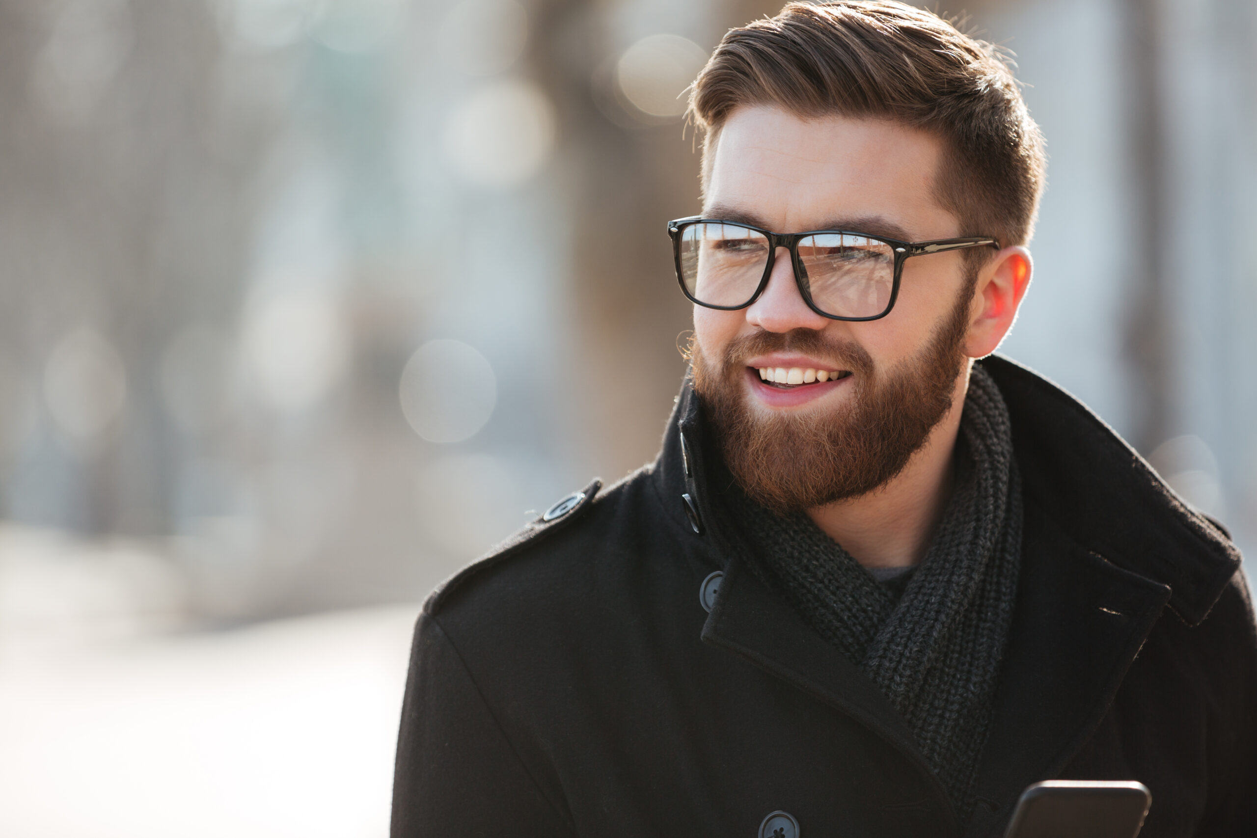 Portrait of happy bearded young man in glasses standing outdoors in winter